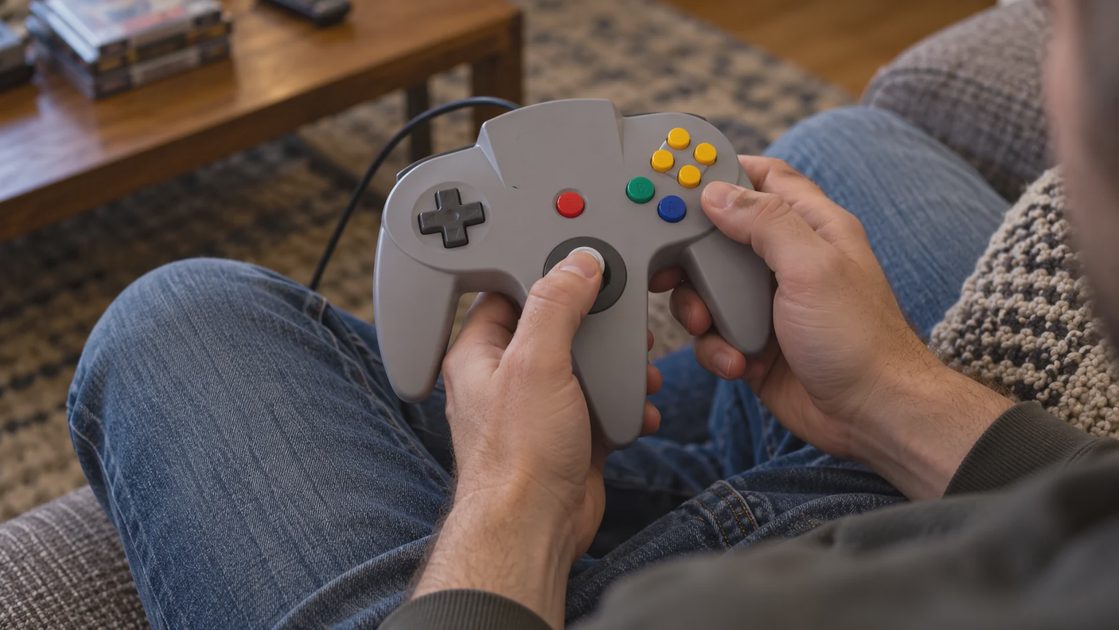 Hands hold a three-pronged controller with the left thumb on its central analog stick and the right hand on the button grip.